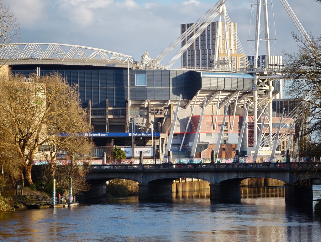 A landscape image showing blue sky, and a river, plus a sports stadium