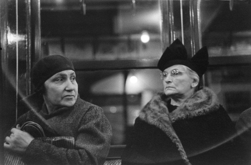 black and white photo of two people on  the subway facing each other