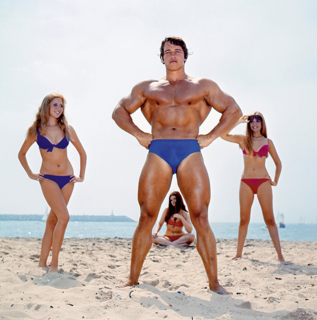 Arnold Schwarzenegger posing with three women in swimwear on a beach