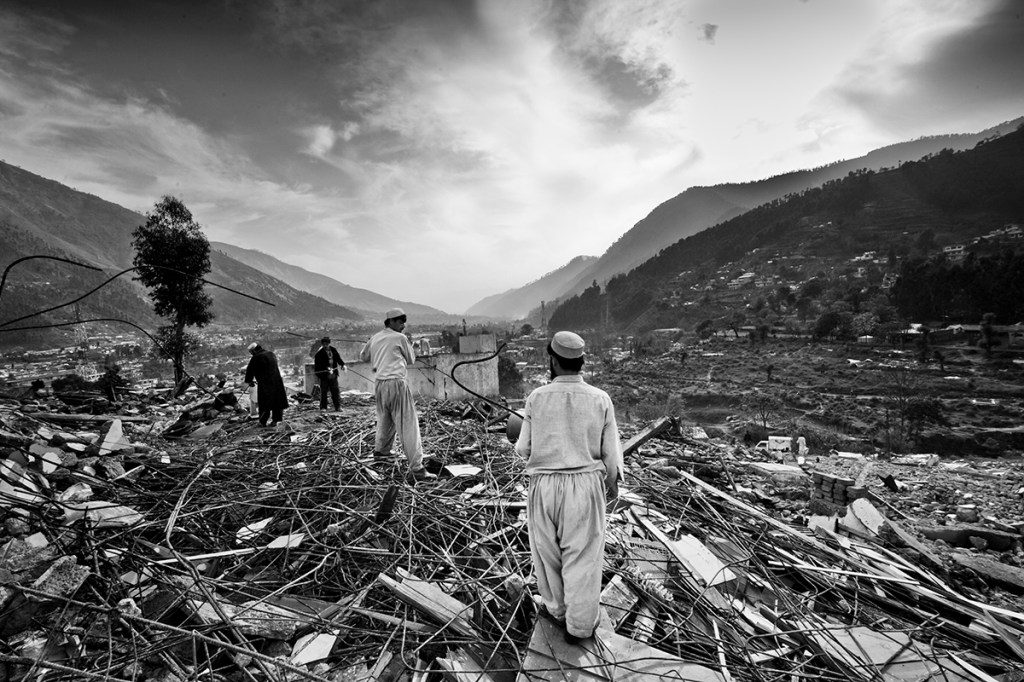 men stood amongst the remains of ballakot earthquake