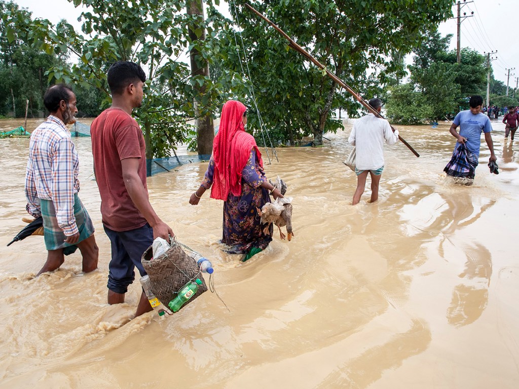 Residents walk through knee-deep floodwater carrying essential belongings in Jhenaigati upazila, Sherpur district, Bangladesh