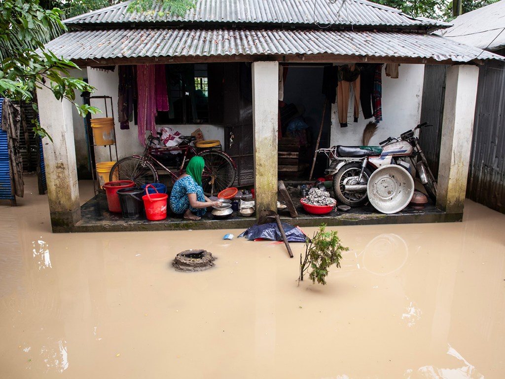 A woman washes household items in floodwater in front of her home in Jhenaigati upazila,