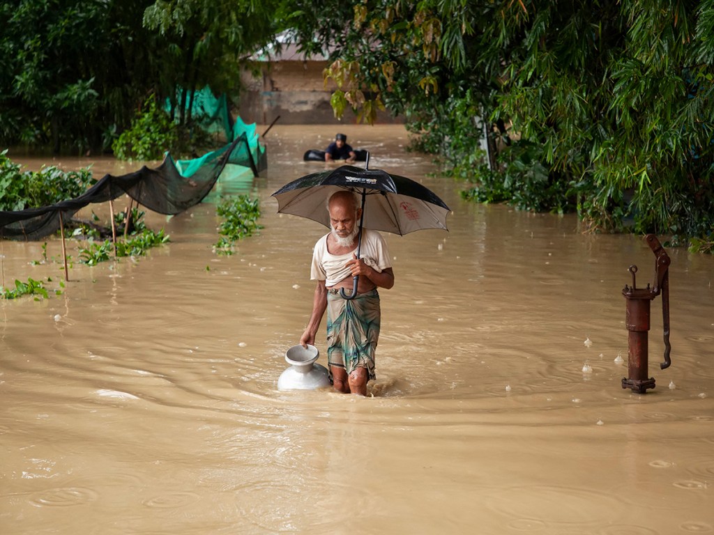 An elderly man walks through floodwater carrying a water container after a nearby tube well stopped functioning during floods in Satkania, Chattogram