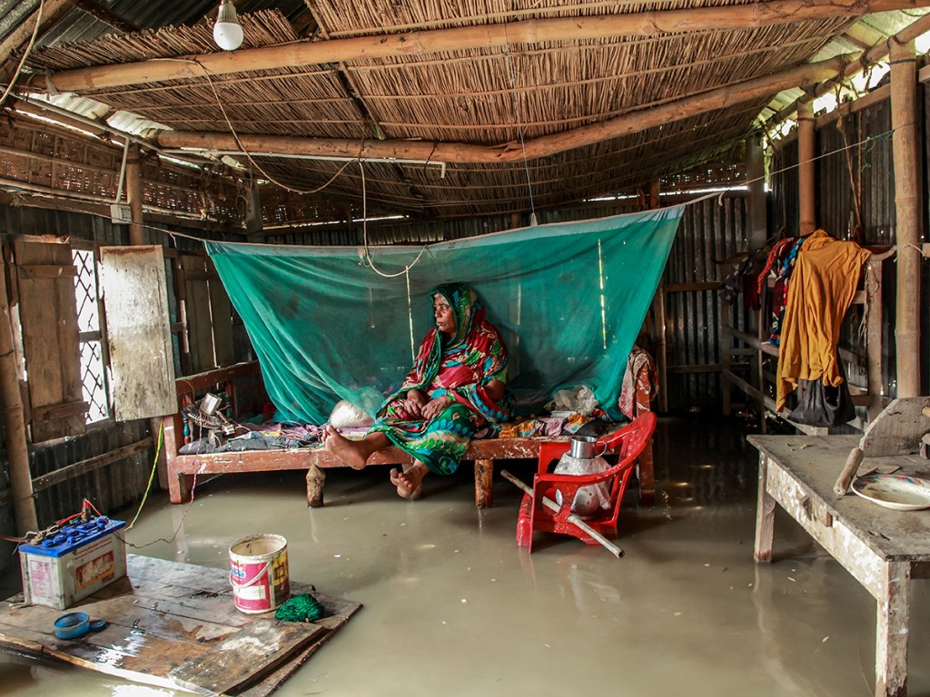 A sick woman sits inside a partially submerged house during severe flooding in Jatrapur Union, Kurigram district, Bangladesh,