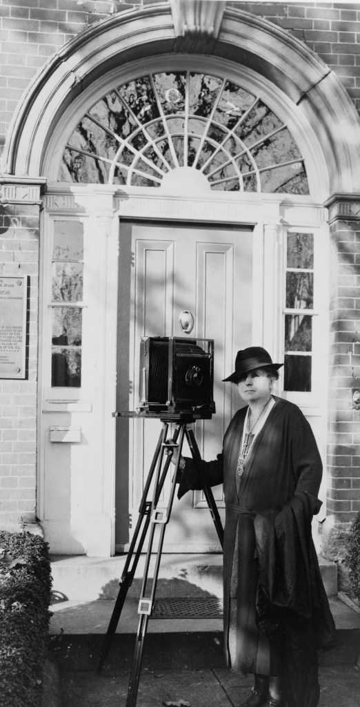 A full-length self-portrait of Frances Benjamin Johnston with camera, 1930-1940