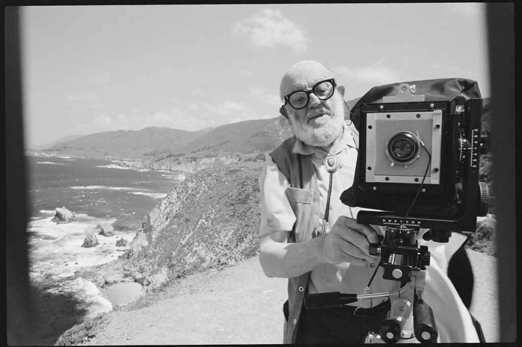 Photographer Ansel Adams stands on a bluff above the Pacific Ocean. He adjusts the settings on his camera. (Photo by © Roger Ressmeyer/CORBIS/VCG via Getty Images)
