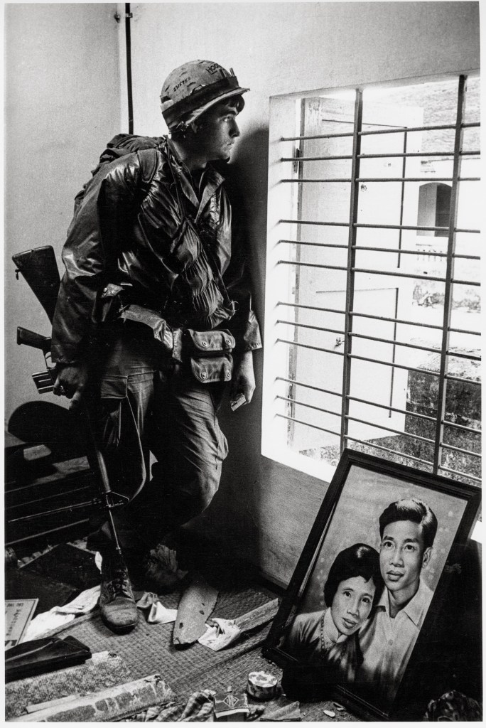 “American soldier in an abandoned home sheltering from sniper fire. Many homes in Hué had been owned by civil servants, professors
working at the local university and other intellectuals or political party members. Before the arrival of the
Americans, the North Vietnamese forces captured Hué in January 1968 and carried out summary executions and the mass murder of 2,800–6,000 people” © Don McCullin