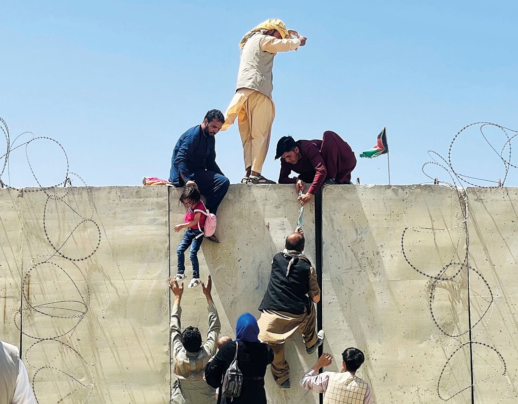 A chaotic aerial scene showing civilians climbing a concrete wall at Kabul International Airport to flee the city in 2021.