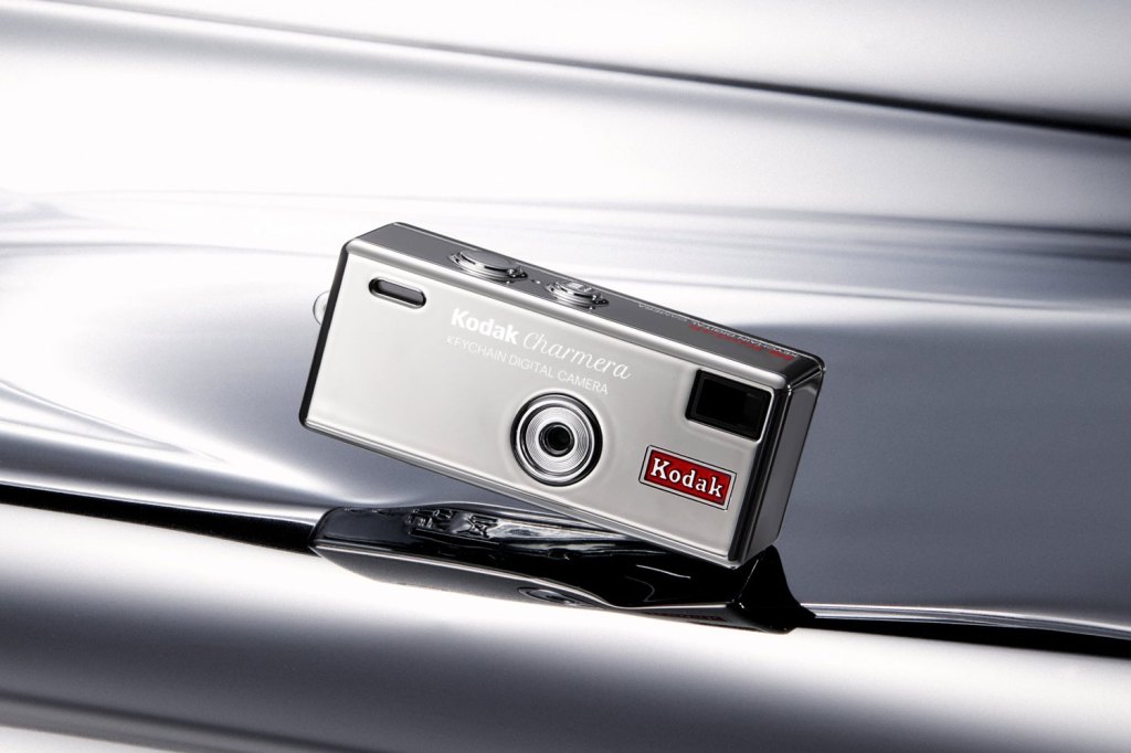 Kodak Charmera chrome floating above a pool of silver liquid