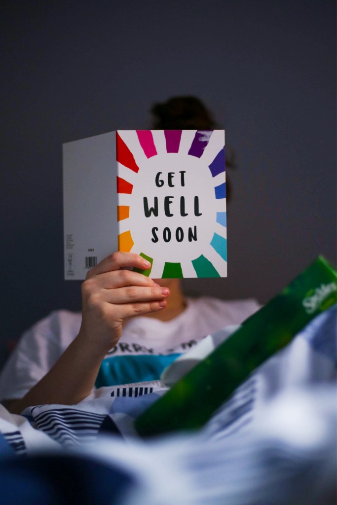 girl holding a get well soon card over her face