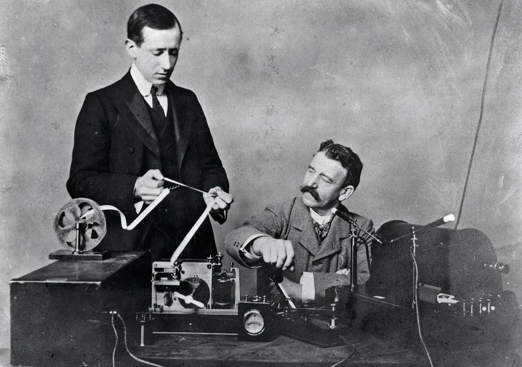 Black and white archival photo of Italian inventor Guglielmo Marconi and his assistant receiving wireless signals in the early 1900s.