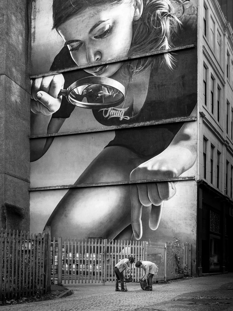 photo of two people bent over in front of street art