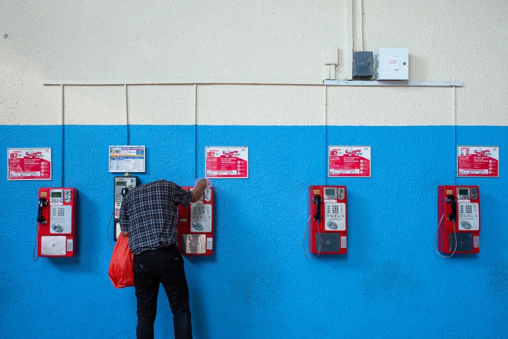 person bent over telephone on the wall