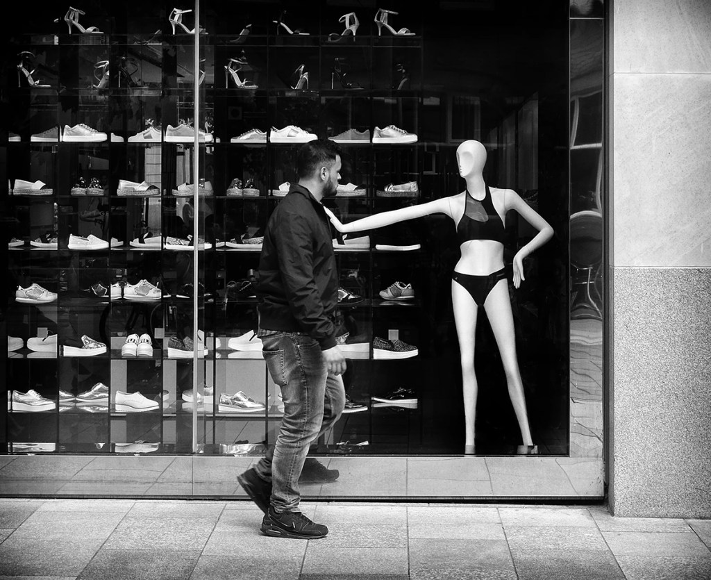 person walking past a shop with model in the window