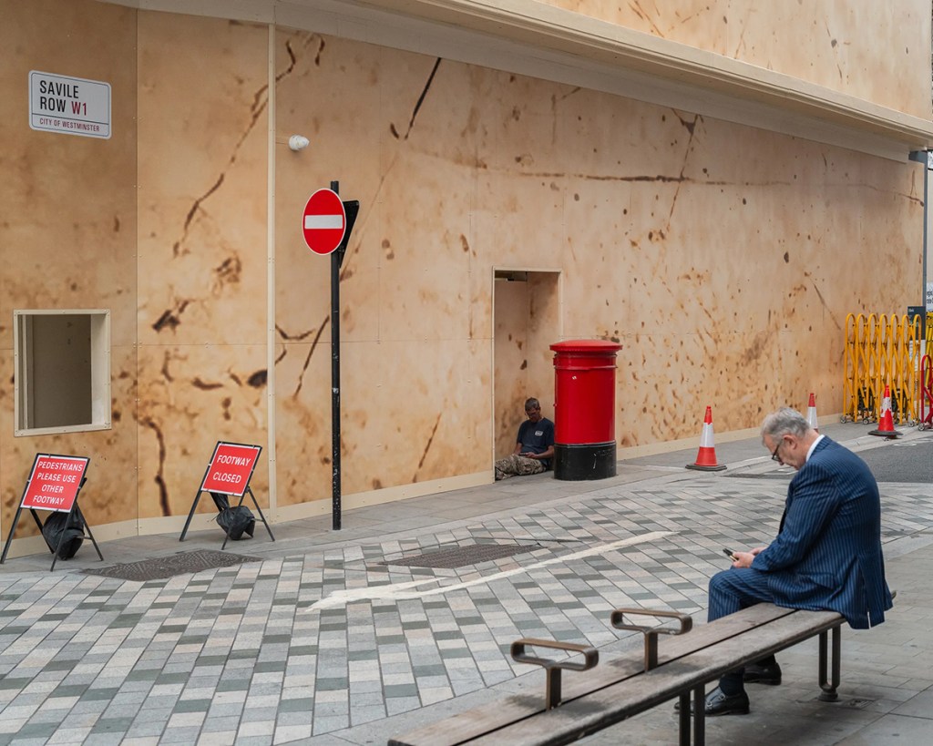 photo of a person sat on a bench looking at phone opposite person sat on the floor looking at phone