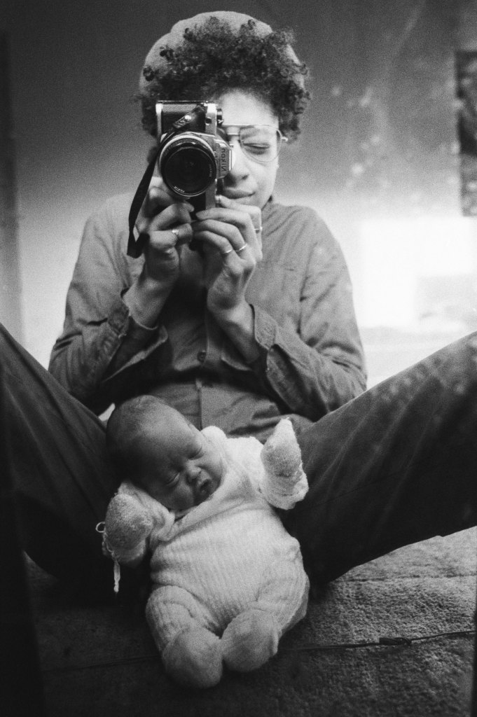 Woman taking a self portrait in a mirror with a baby sitting in between her legs