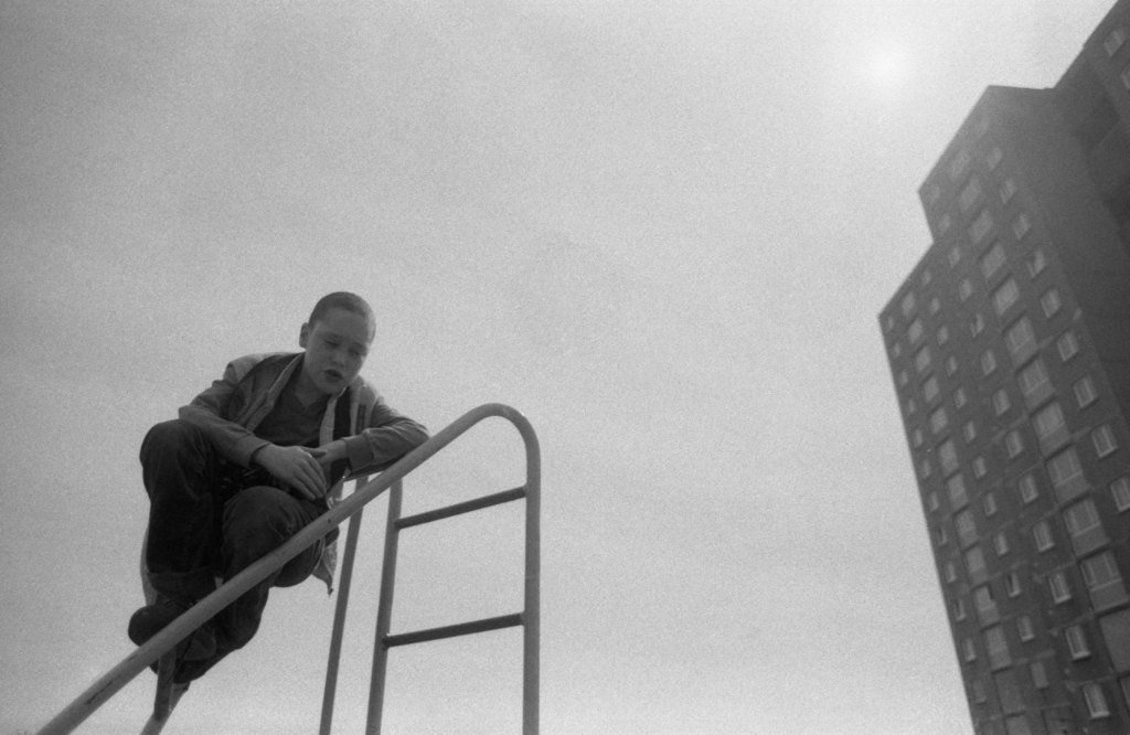 A child on top of a climbing frame, and a high rise building. Part of Sandra George street photography exhibition