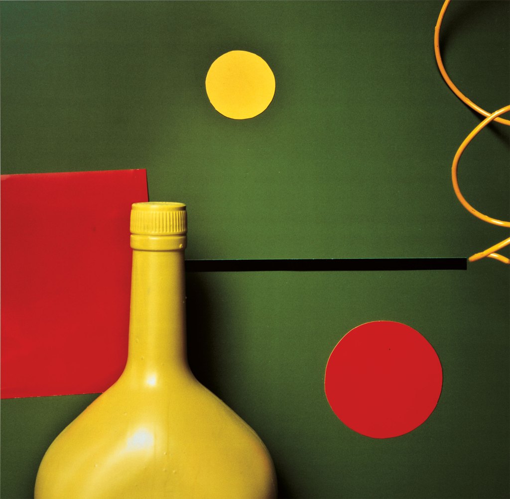 Colour photograph of the top of a yellow bottle against a green background.
