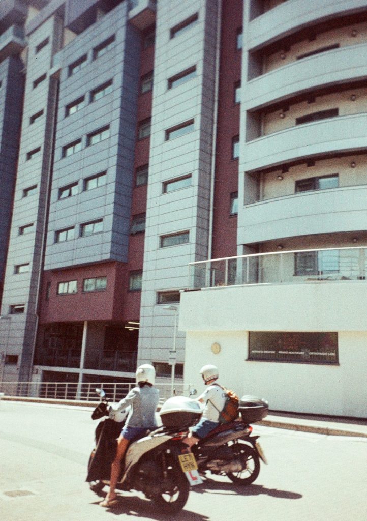 Sample photograph from the Lomography Half-frame Simple Use Camera, shot on LomoChrom Classicolor 200 film showing two people parked on scooters in front of flats