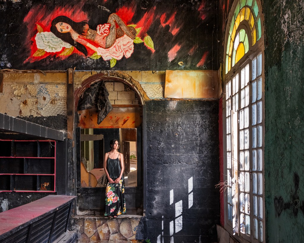 A woman stands in an archway with a large windoe illuminating her