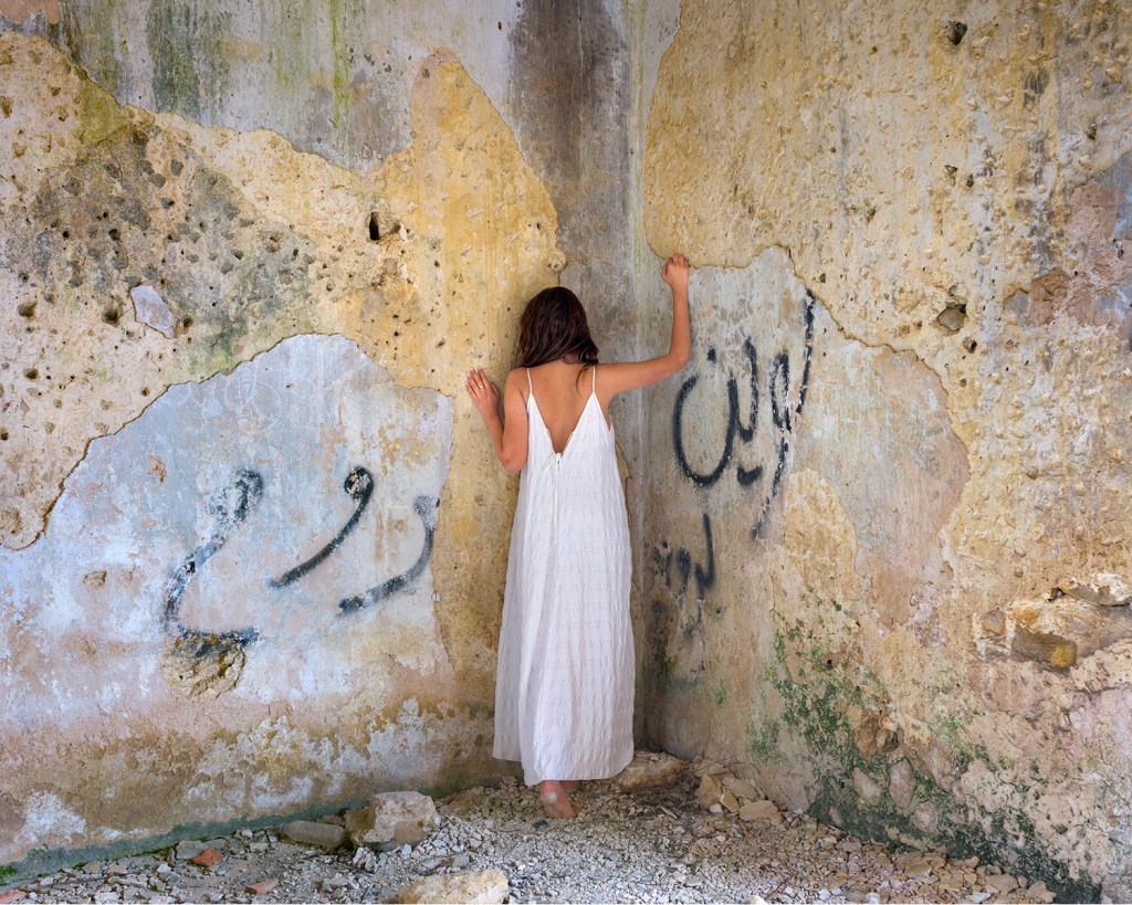 A woman in white dress stands in the corner of a derelict house