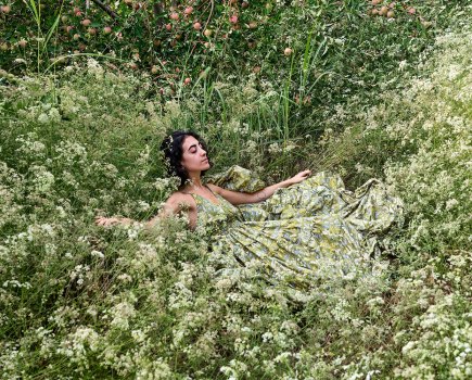 A woman wearing a pale green dress lays in a field of white flowers