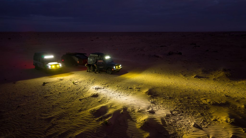 Two touring cars with their headlights on at night in the desert