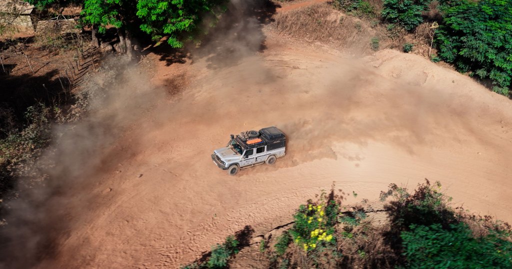 a car speeds along a dirt road stirring up plumes of dust
