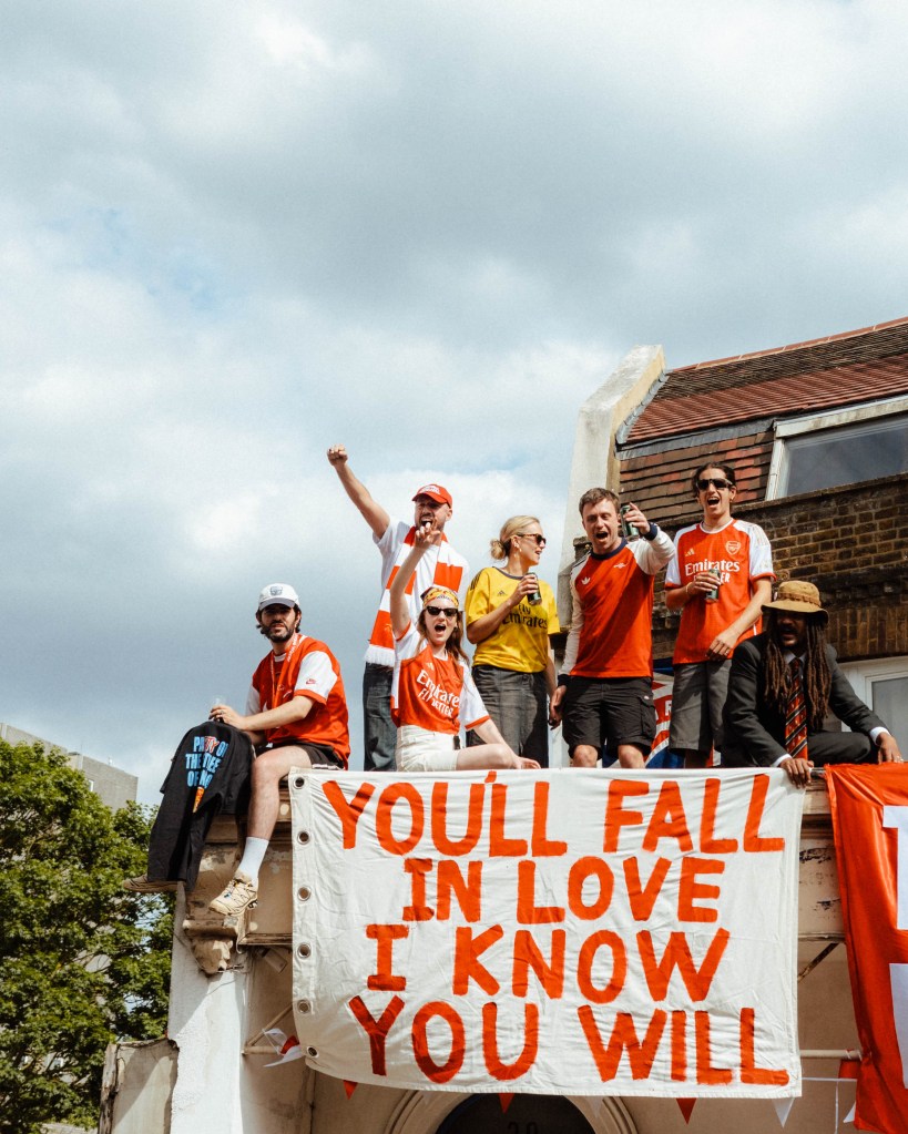 arsenal supporters celebrating premier league win with 'you'll fall in love I know you will' sign