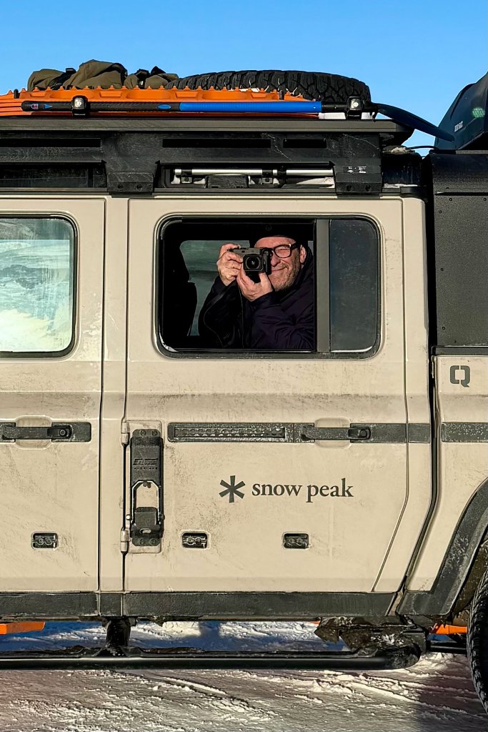 John Balsdon sitting in the back of a car holding a camera up to his eyes