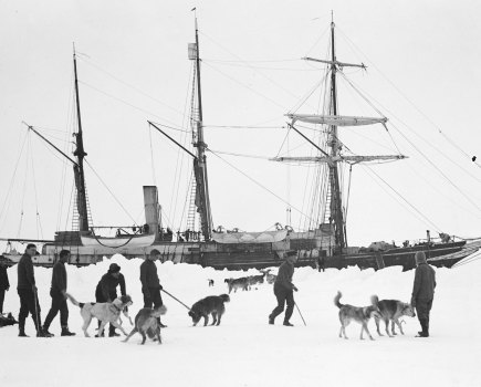 Shackleton’s 1914 Antarctic expedition, a ship ancohred in ice with people in the foreground exercising with dogs