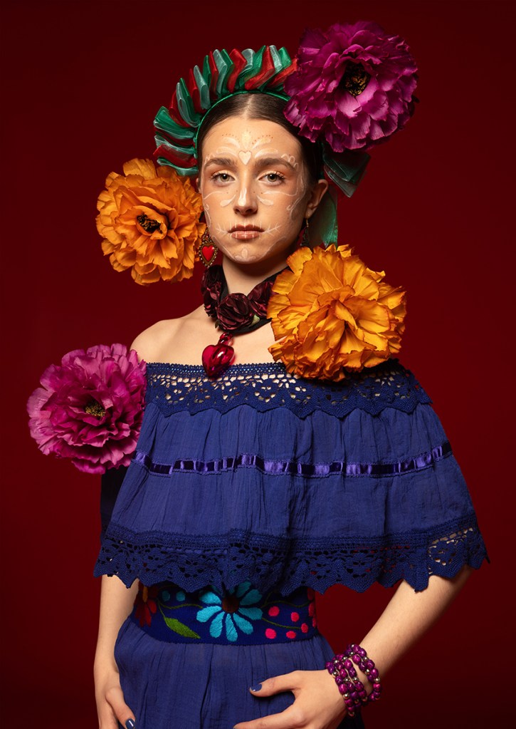'La Catrina' from Soul of Mexico. More than just a representation of death, "La Catrina" serves as a profound connection to Mexican roots and a vibrant celebration of life. This portrait captures the spirited femininity of the Day of the Dead through intricate makeup, handmade paper flowers and jewellery. The two-piece embroidered set from Puebla was sourced from a local Mexican market to support the women artisans who keep traditional folklore and craftsmanship alive. This is further inspired by two icons I've always admired: the enduring passion of Frida Kahlo symbolised by the deep blue dress colour, and a childhood fascination with traditional "Michoacán" dolls represented through the ribbon headpiece. By drawing on these influences, the piece honours the spirit of the Day of the Dead, a celebration that empowers girlhood and pays tribute to the legacy of female artists