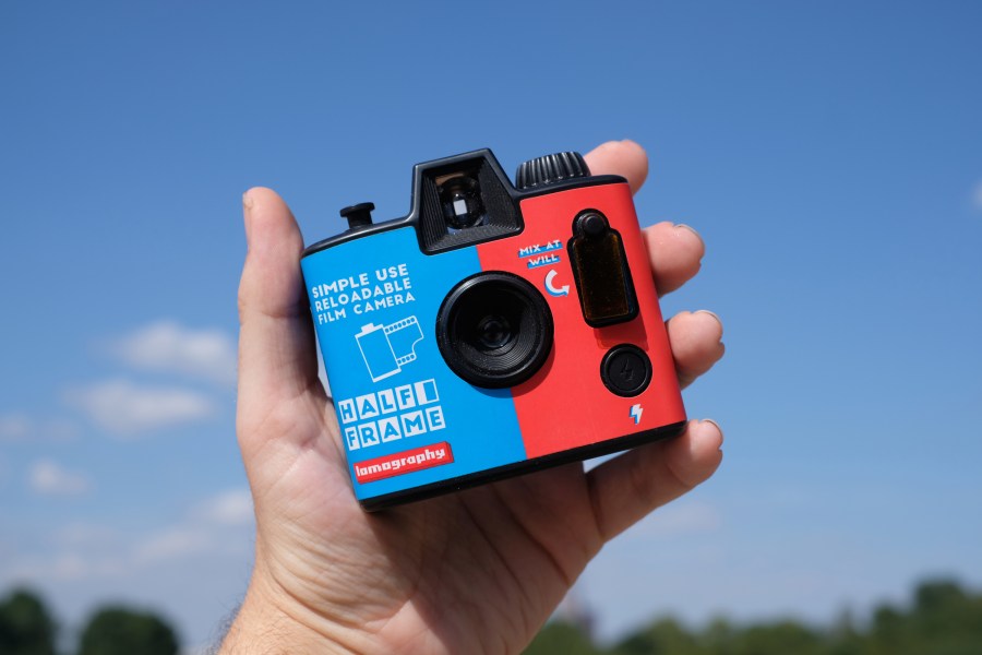 Photograph of the Lomography Half-frame Simple Use Camera held in one hand, facing front with lens and flash control visible