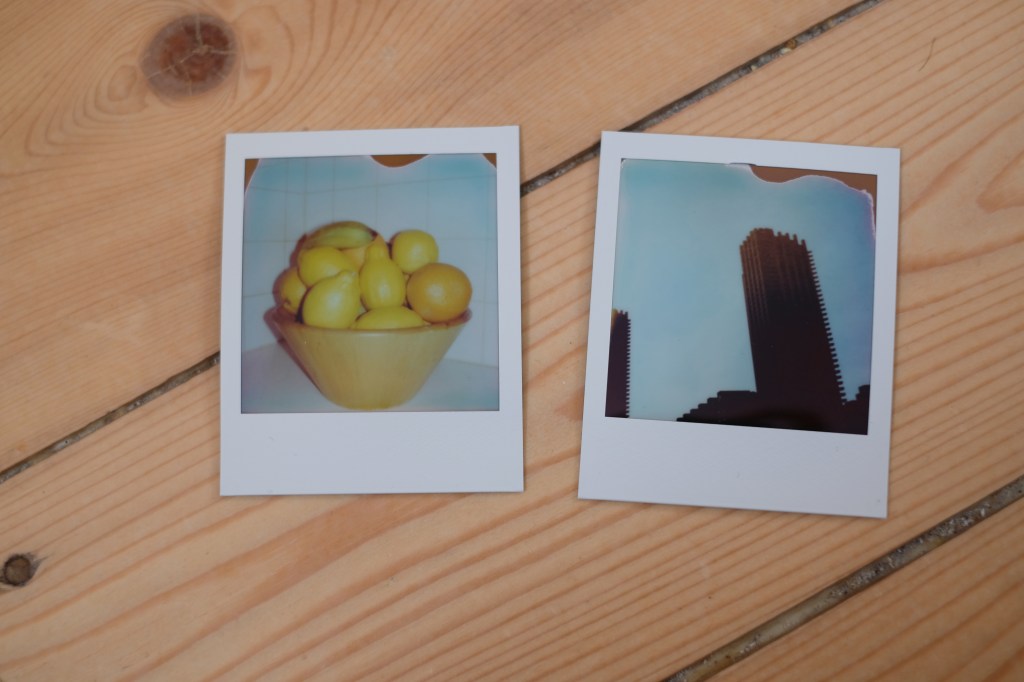 Polaroid Go photographs of a fruit bowl and the Barbican tower, both with marks from what appears to be heat damage