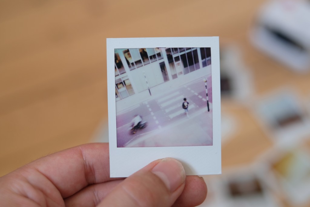 Polaroid Go photograph of a zebra crossing, taken from above, with a pedestrian and blurred cyclist passing