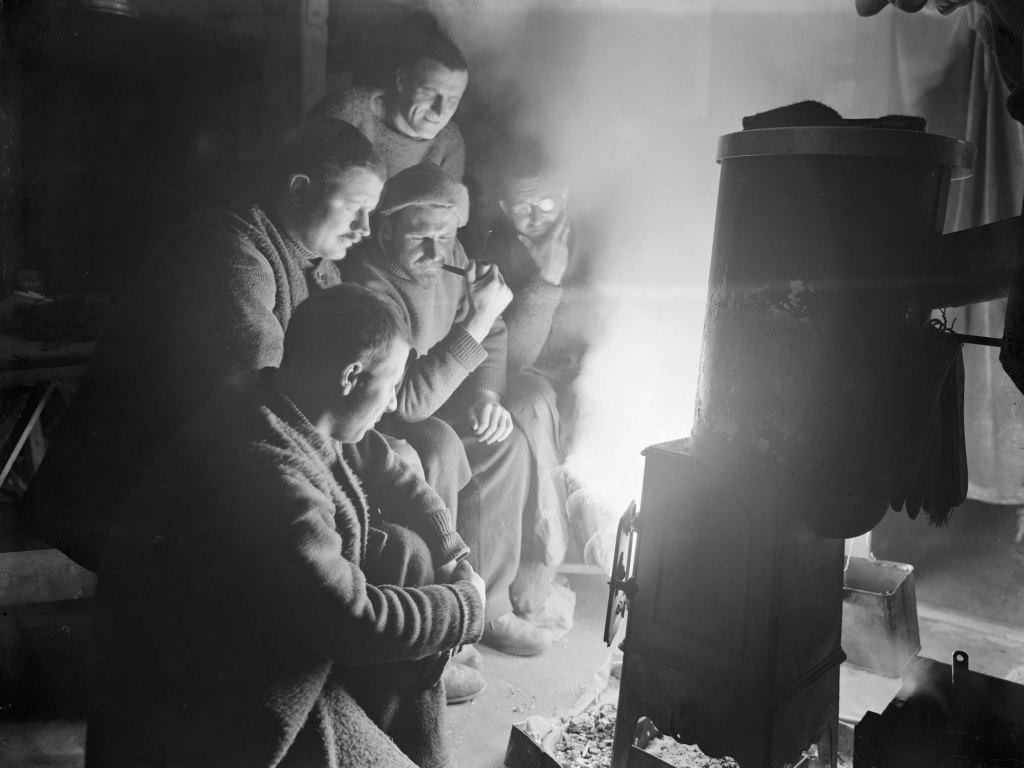 Men huddled together in front of a stove which light illuminates their faces at night
