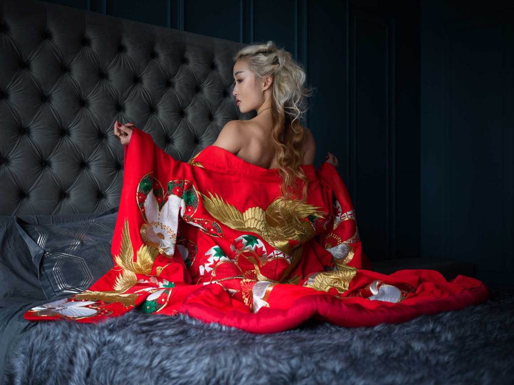 Boudoir photo of a woman siting on top of a bed in a red kimono night gown