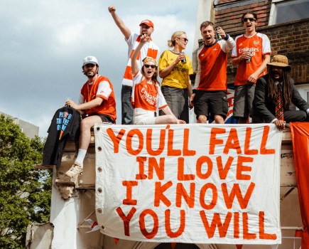 arsenal supporters celebrating premier league win with 'you'll fall in love I know you will' sign