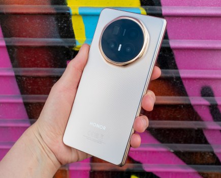 Honor Magic V6 foldable phone in hand. Photographed against a pink graffiti wall.