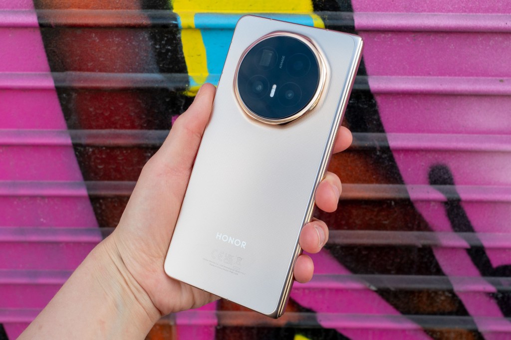 Honor Magic V6 foldable phone in hand. Photographed against a pink graffiti wall.