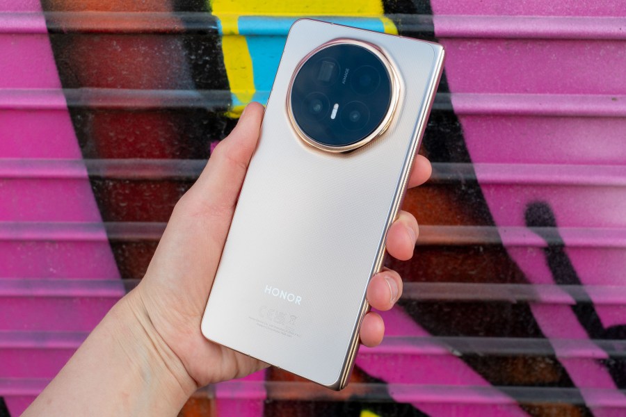 Honor Magic V6 foldable phone in hand. Photographed against a pink graffiti wall.