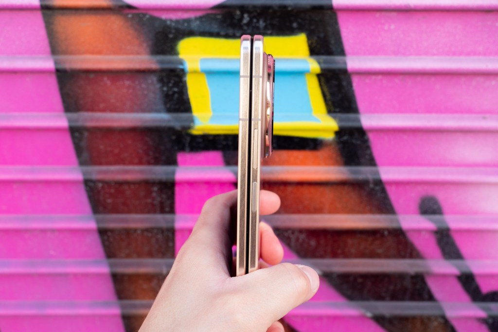 Honor Magic V6 foldable phone side view, in hand. Photographed against a pink graffiti wall.